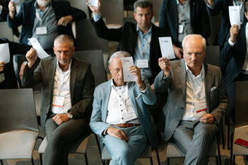 Menschen im Publikum halten einen Folder in die Luft